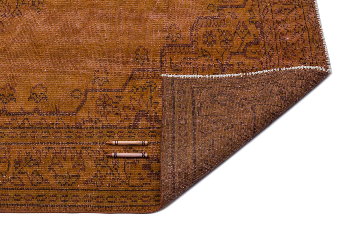Rust-colored vintage rug with a dark brown floral border and a folded corner revealing the darker underside.