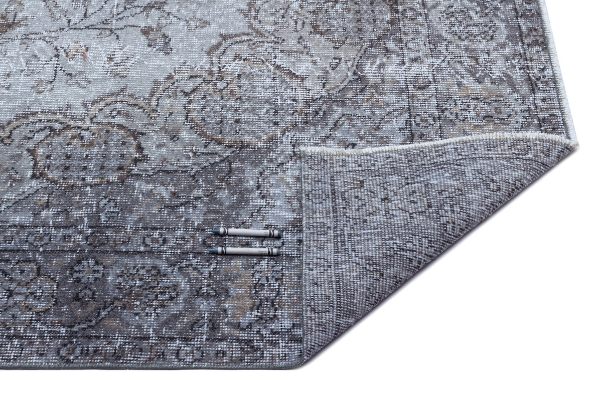 Grey and charcoal distressed traditional rug with a floral medallion pattern, shown with a corner folded over.