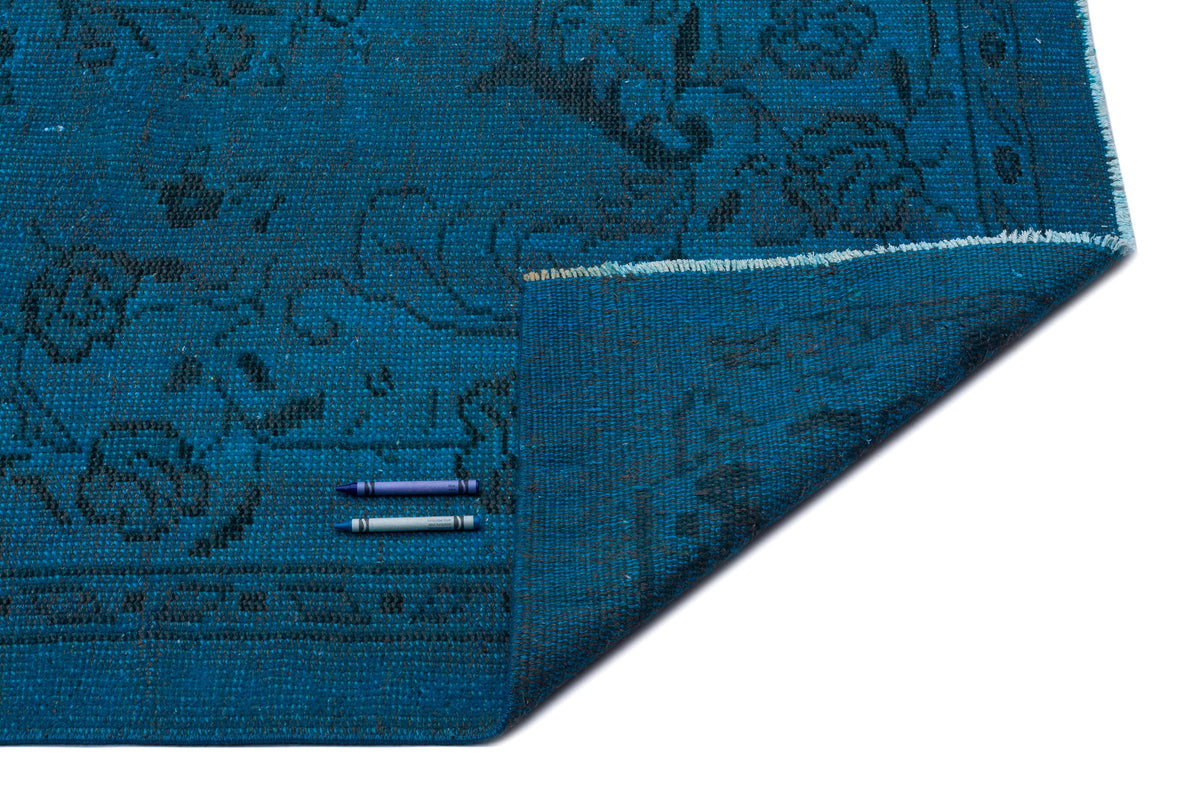 Teal rug with a dark grey floral medallion pattern, shown with a folded corner on a white background.