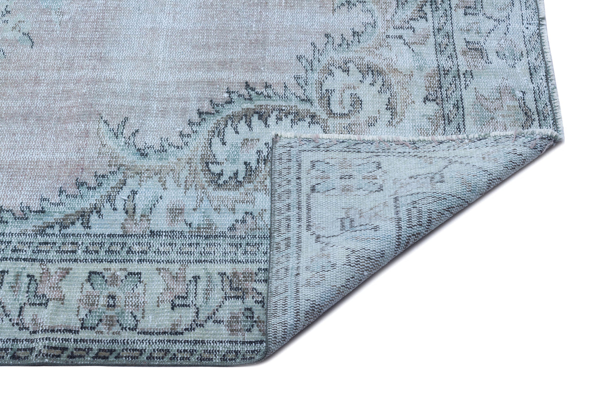 Distressed light blue and beige rug with a traditional floral medallion pattern, shown with a corner folded over.