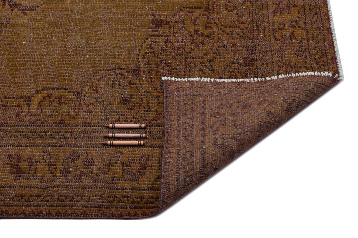 Distressed brown rug with a faded floral medallion pattern, shown with a corner folded back and three crayons for scale.