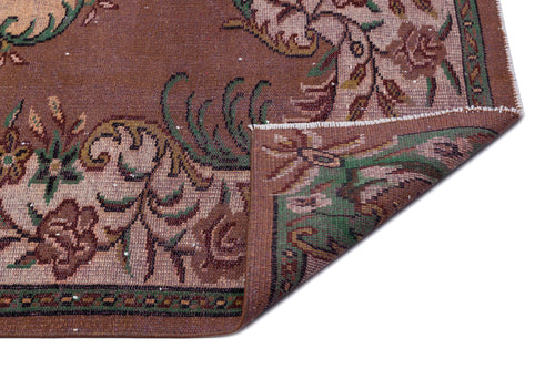 Load image 1 in gallery view. Brown traditional rug with a floral pattern in green and beige, shown with a corner folded over on a white background.