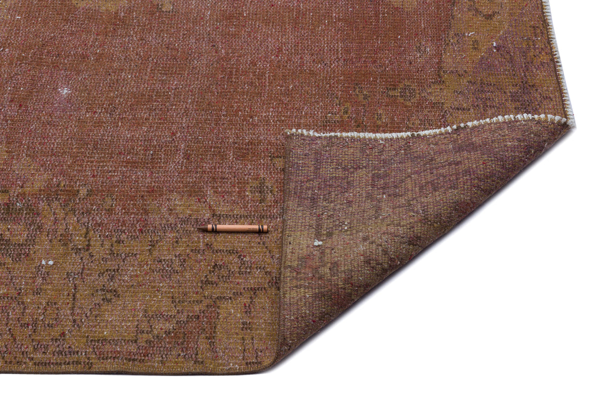 Distressed rust and ochre vintage-style rug with a folded corner revealing the woven backing and a small brown crayon.