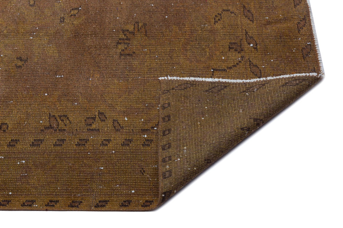 Distressed brown rug with a faded geometric pattern and a folded corner showing the woven backing.