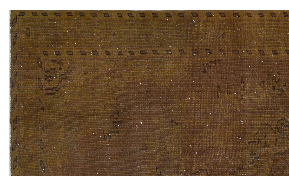 Distressed brown rug with a faded geometric border and scattered white flecks on a white background.