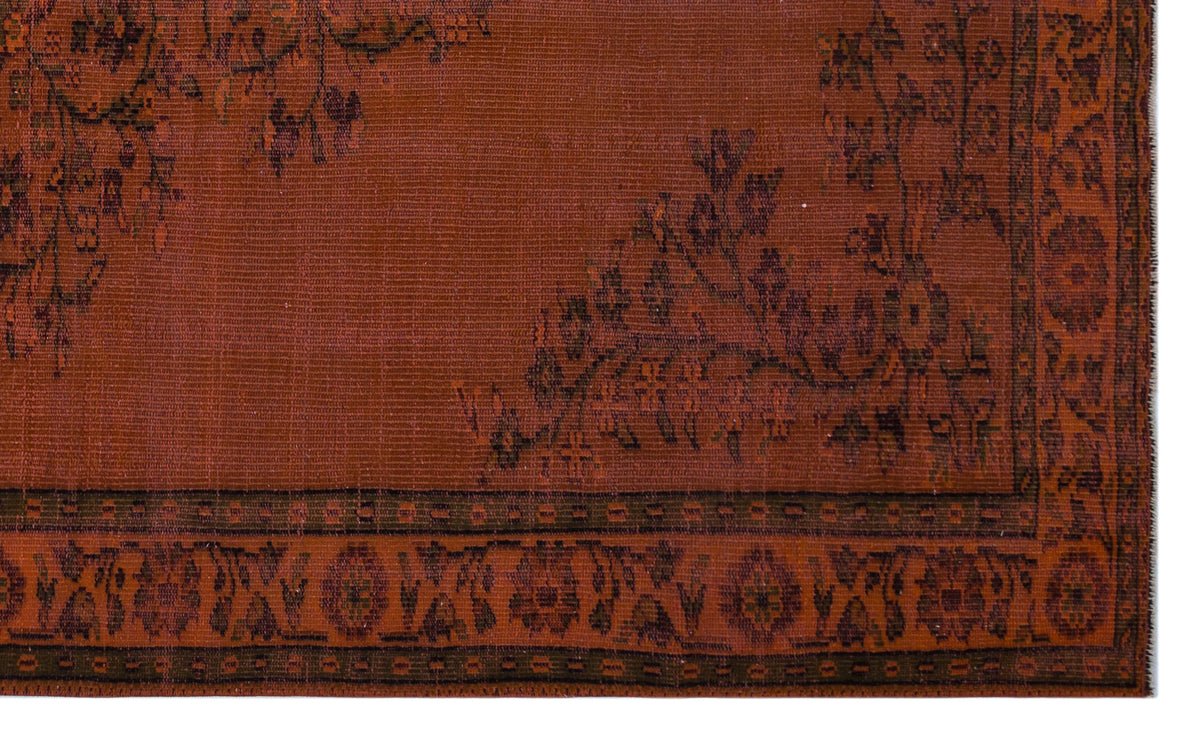 Rust-colored rug with a dark brown floral vine pattern and a geometric border.