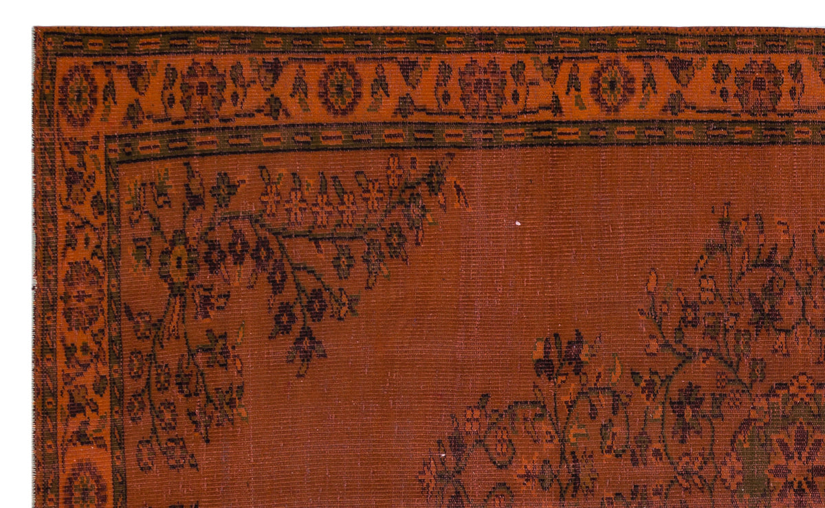 Rust-colored traditional rug with a dark green floral border and central botanical motifs.