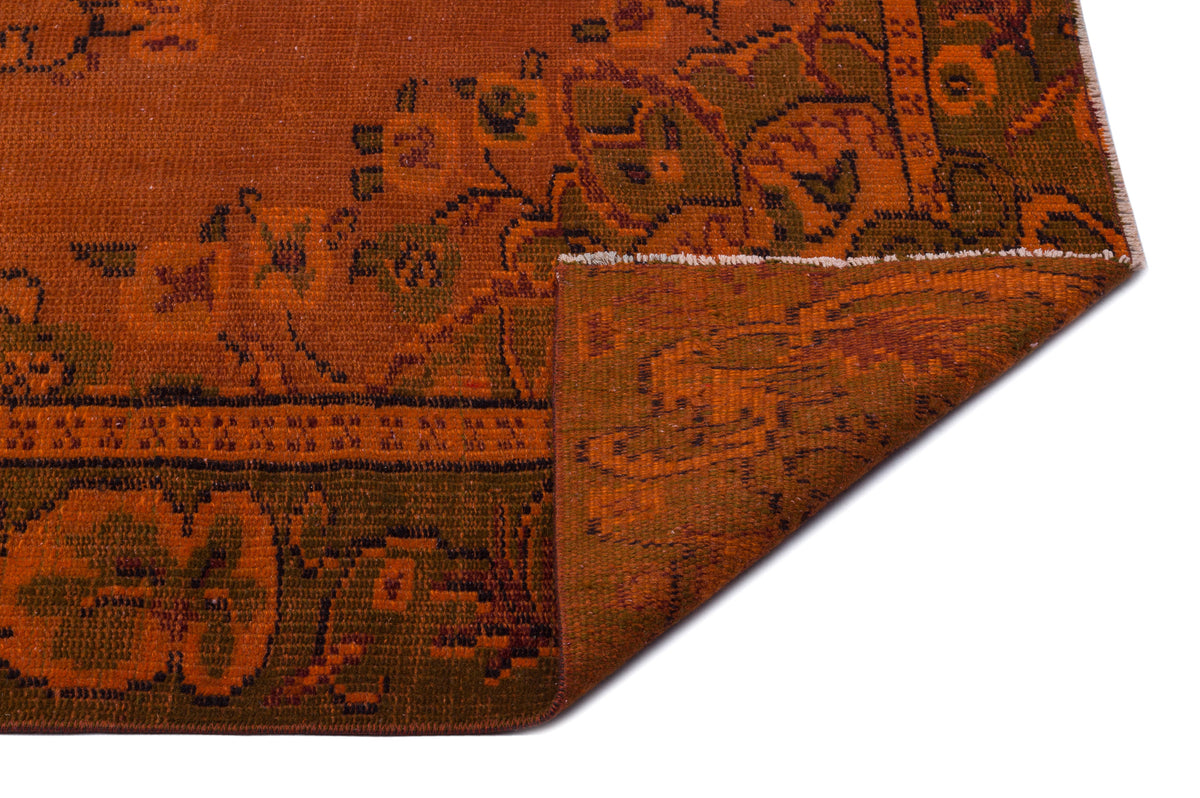 Rust orange and olive green traditional rug with a floral medallion pattern, shown with a corner folded over.