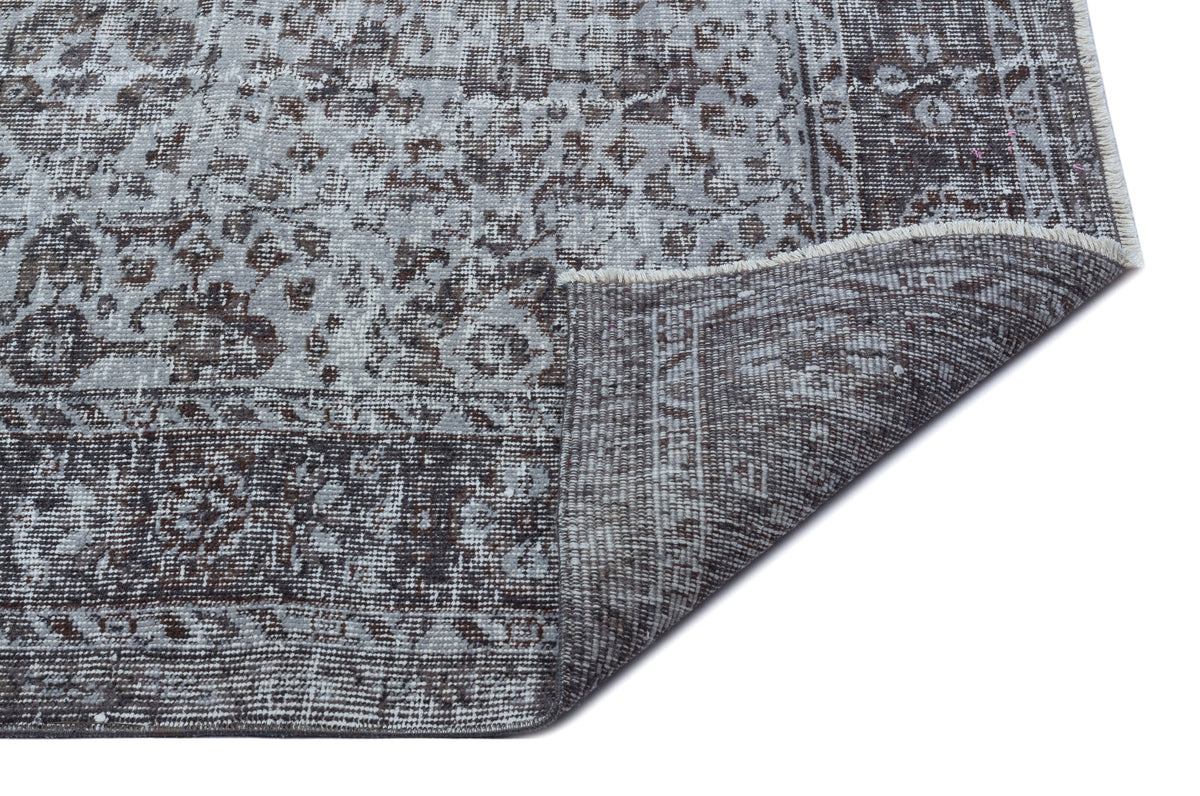 Grey and charcoal distressed rug with a traditional floral medallion pattern, shown with a corner folded over.