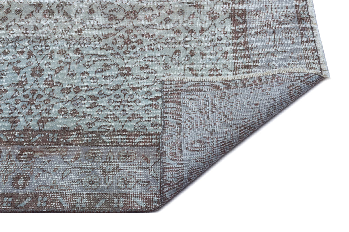 Light blue and brown distressed rug with a traditional floral pattern, shown with a corner folded to reveal the backing.