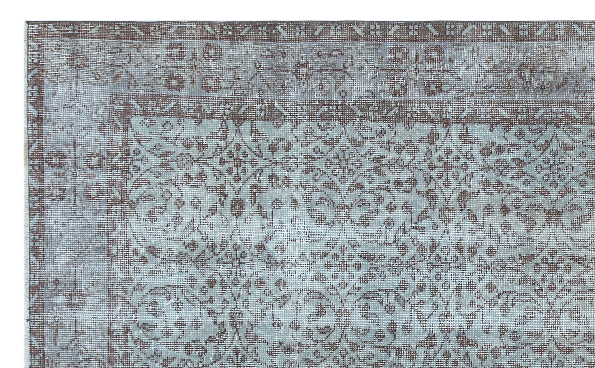 Distressed light blue and brown rug with a traditional floral medallion pattern and a geometric border.