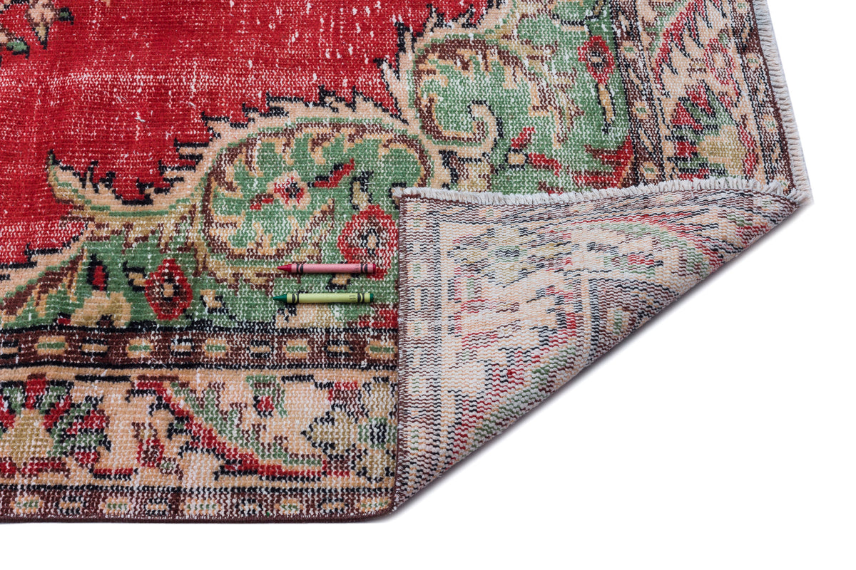 Distressed red and green traditional medallion rug with a folded corner showing the woven backing and two crayons.