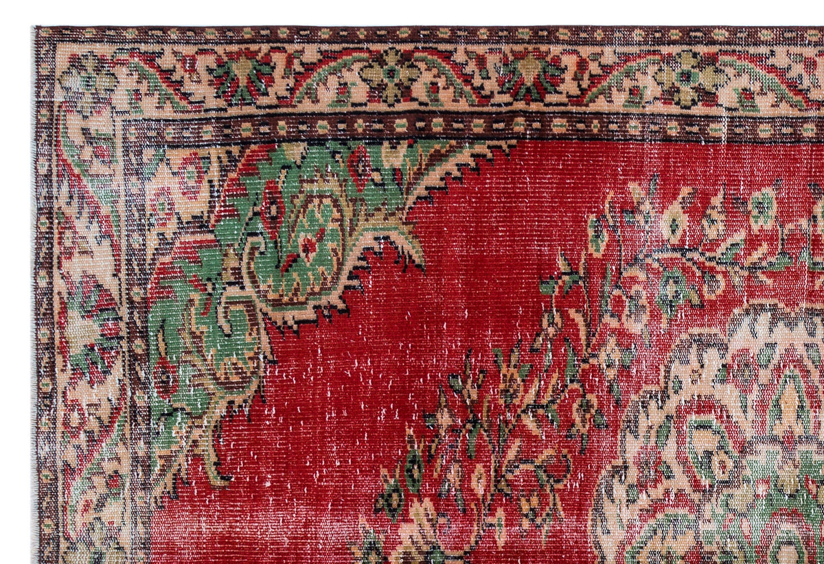 Distressed red rug with a traditional green and beige floral border and central medallion pattern.