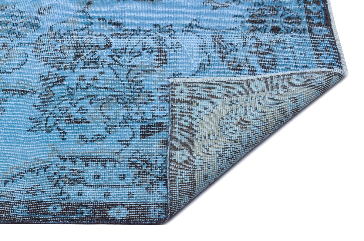 Bright blue distressed rug with a dark grey traditional floral pattern and a folded corner showing the backing.