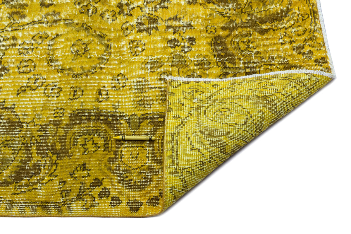 Mustard yellow and olive green distressed traditional rug with a floral medallion pattern, corner folded over.
