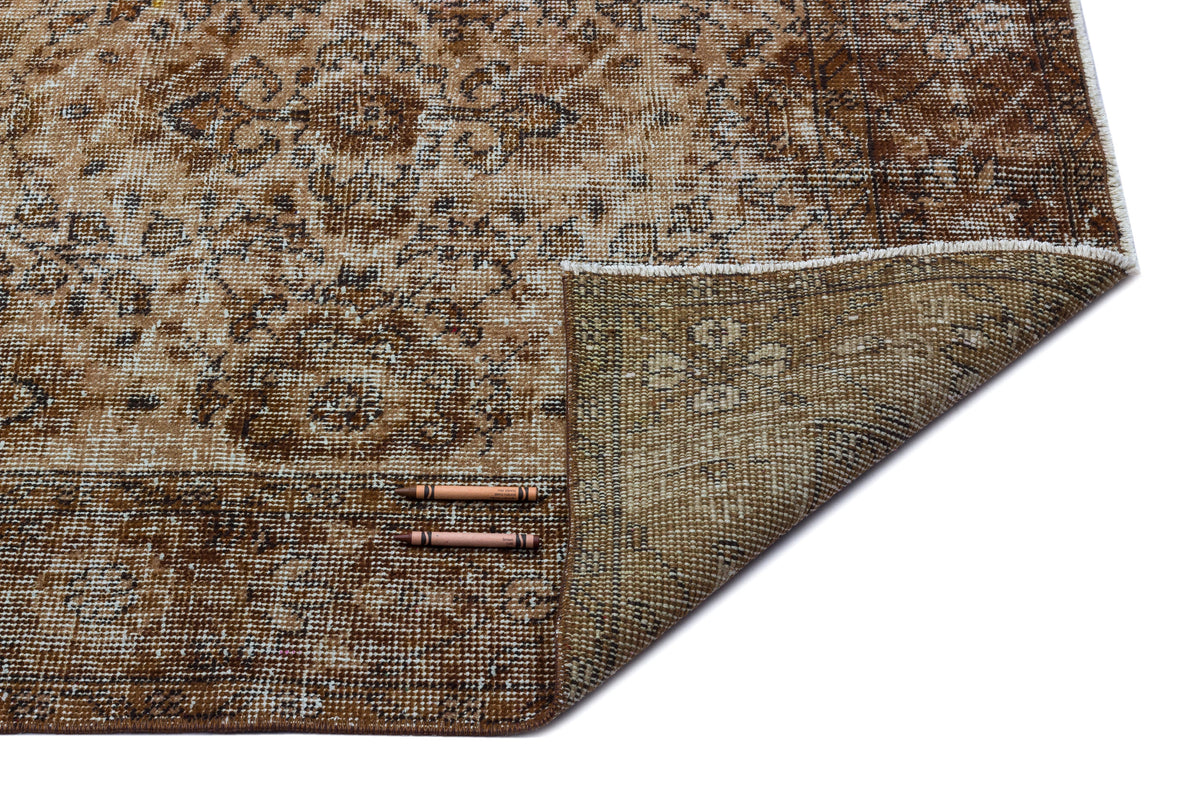 Distressed brown and beige traditional rug with a floral medallion pattern, shown with a corner folded over.