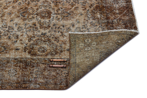 Load image 1 in gallery view. Distressed brown and beige traditional rug with a floral medallion pattern, shown with a corner folded over.