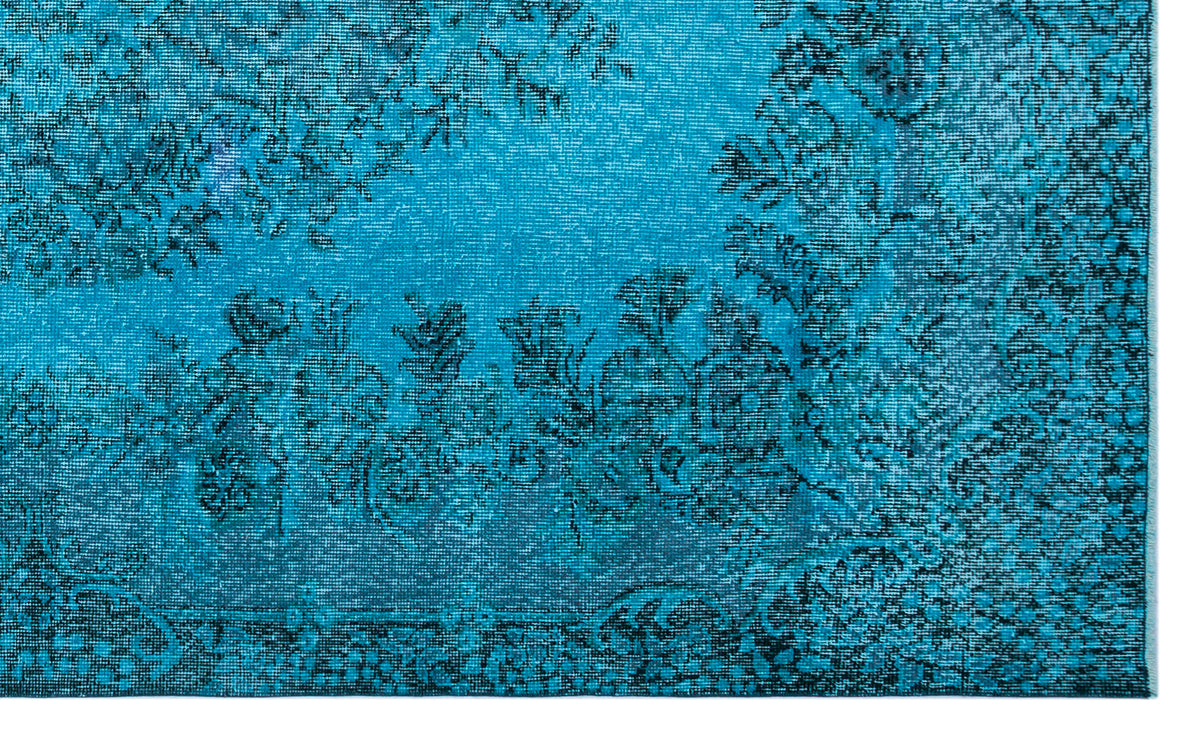 Bright turquoise rug with a distressed black floral medallion pattern.