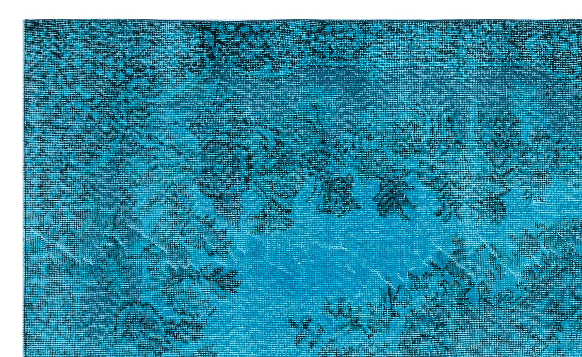 Bright turquoise rug with a distressed black floral and vine pattern.