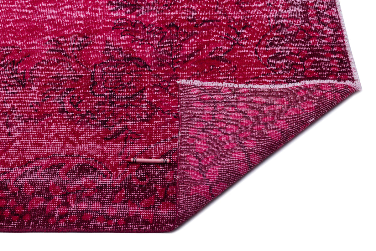 Magenta and dark red distressed floral rug with a folded corner showing the underside texture on a white background.