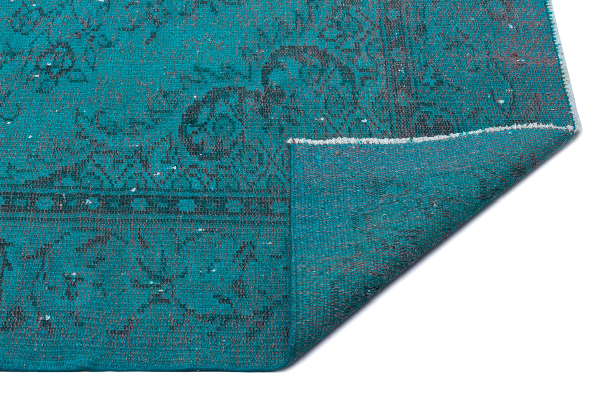 Teal and charcoal distressed traditional rug with a folded corner revealing the woven backing.