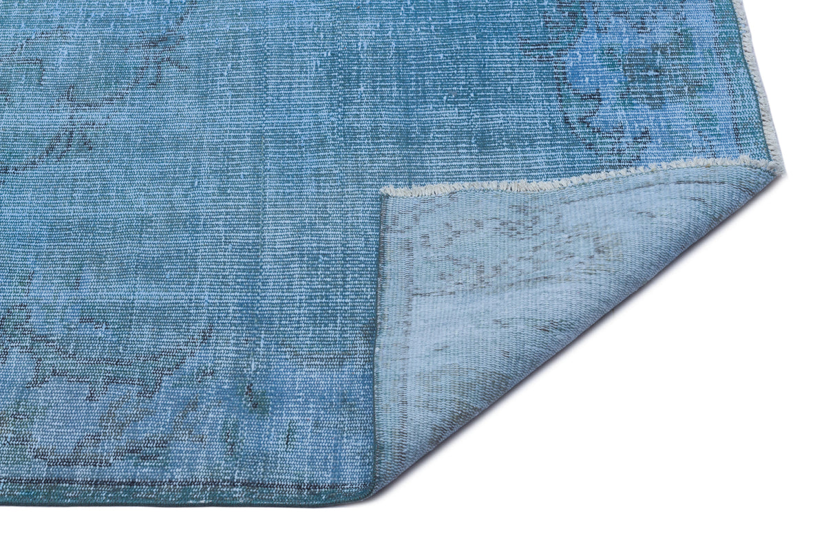 Distressed blue area rug with a faded traditional medallion pattern and a folded corner showing the backing.