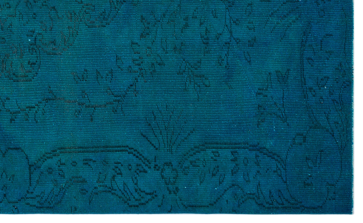 Teal rug with a subtle, dark-toned floral and vine pattern in a flat-weave texture.