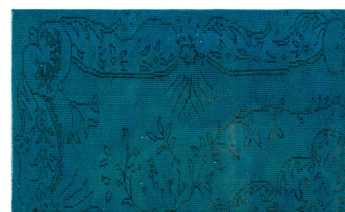 Teal rug with a subtle, dark-toned floral and vine pattern on a white background.
