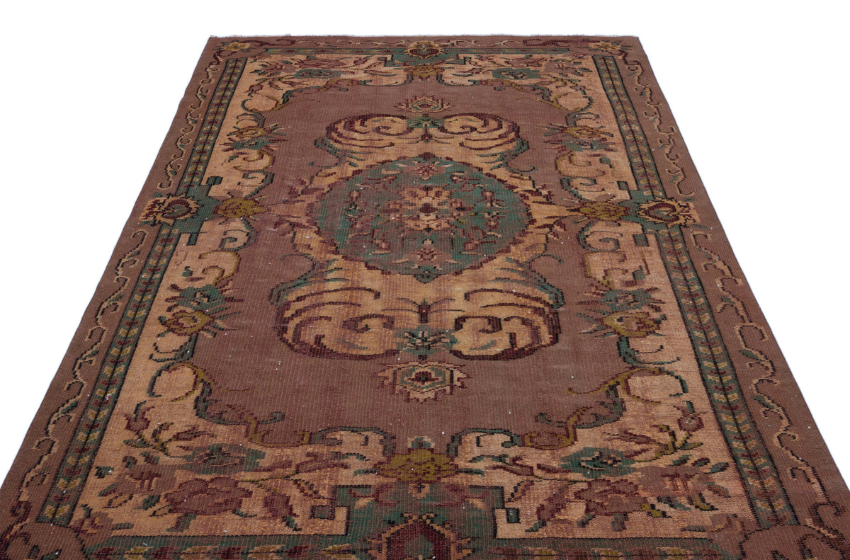 Brown traditional rug with a central green and tan floral medallion and ornate border patterns on a white background.