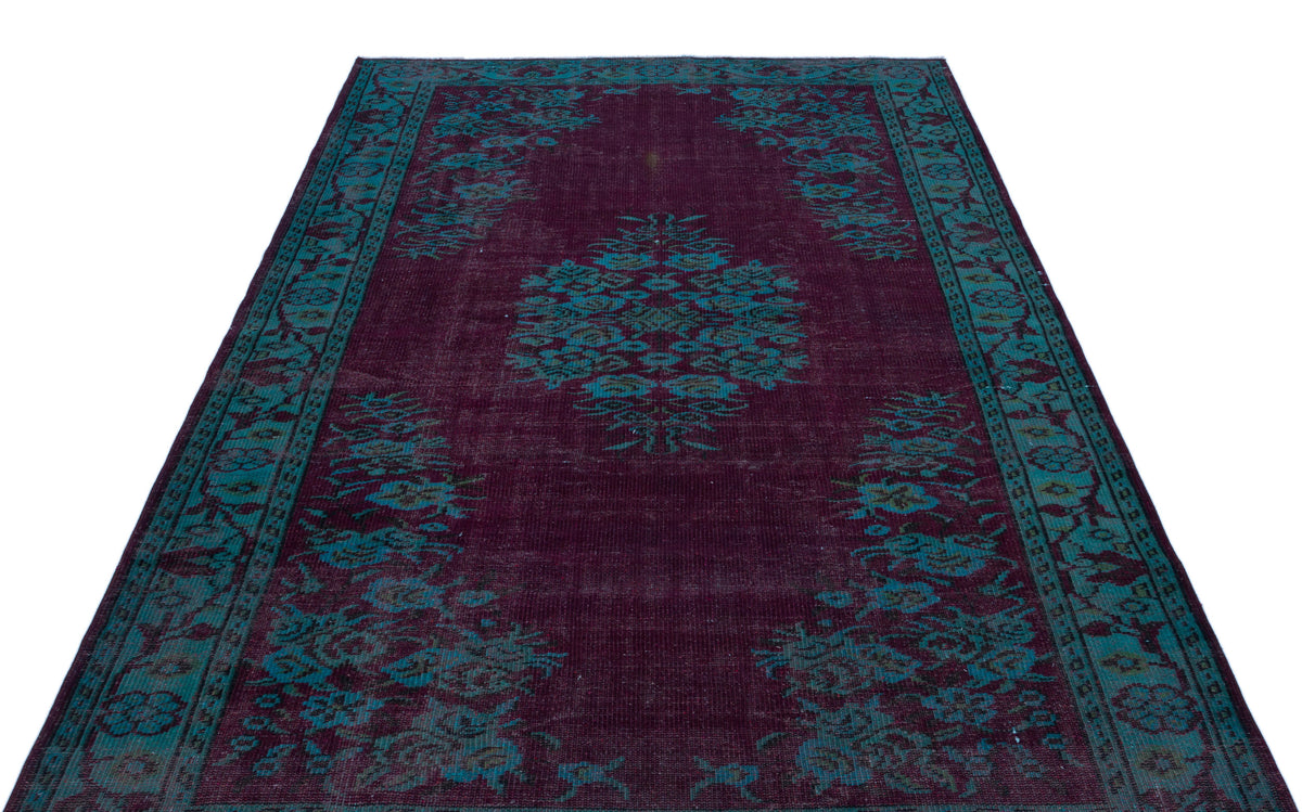 Deep purple rug with a teal floral medallion and border pattern on a white background.
