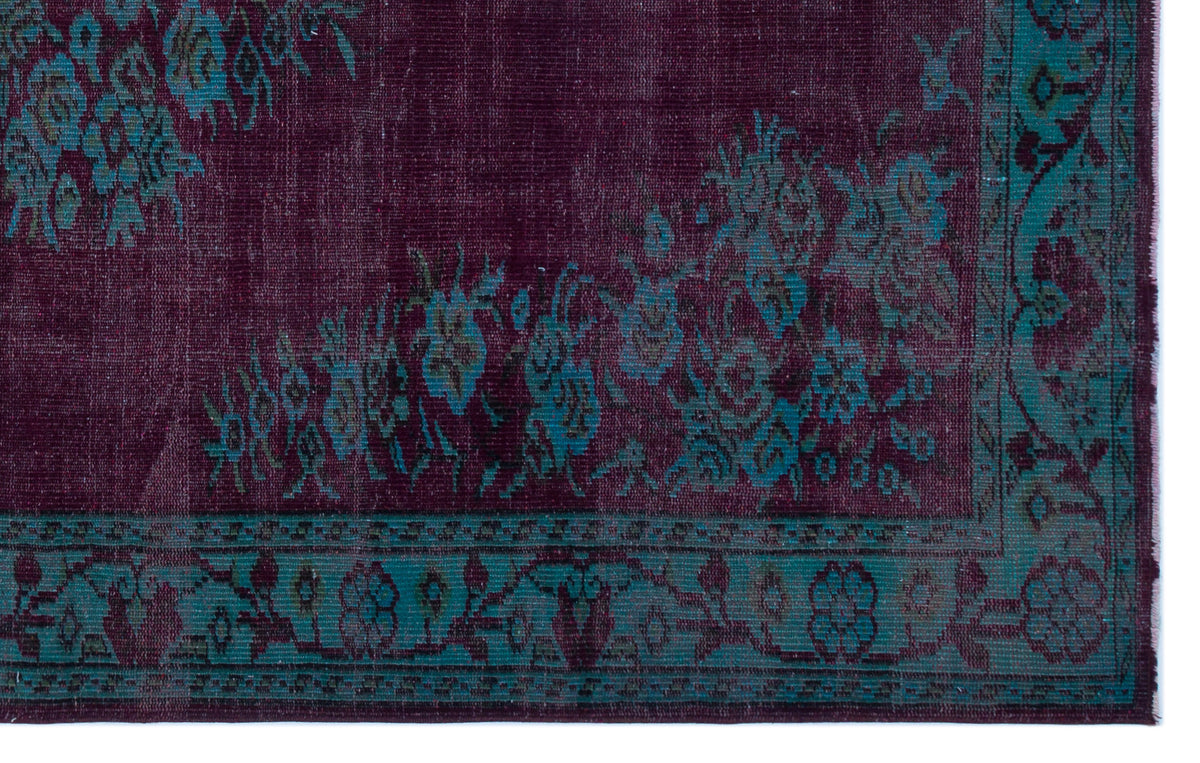 Deep purple distressed rug with teal floral motifs and a decorative border.