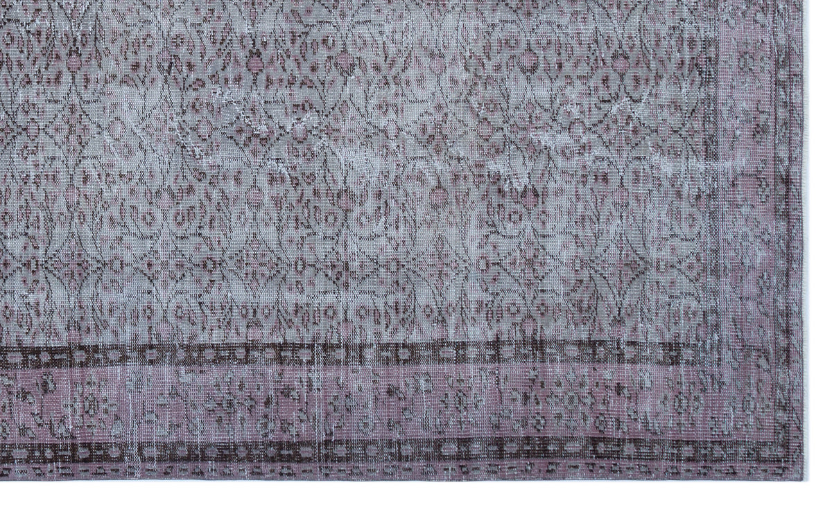 Distressed mauve and grey rug with a traditional floral medallion pattern and a geometric border.