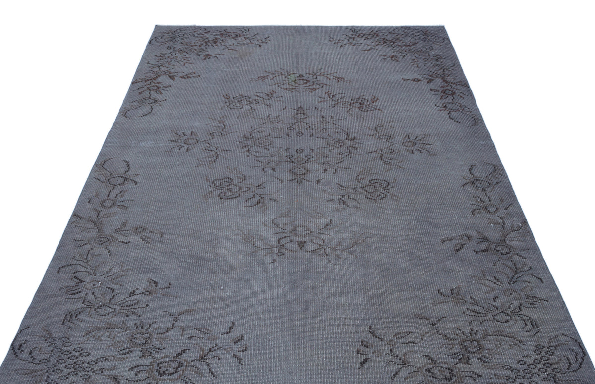 Charcoal grey rug with a faded, dark floral medallion and border pattern on a white background.