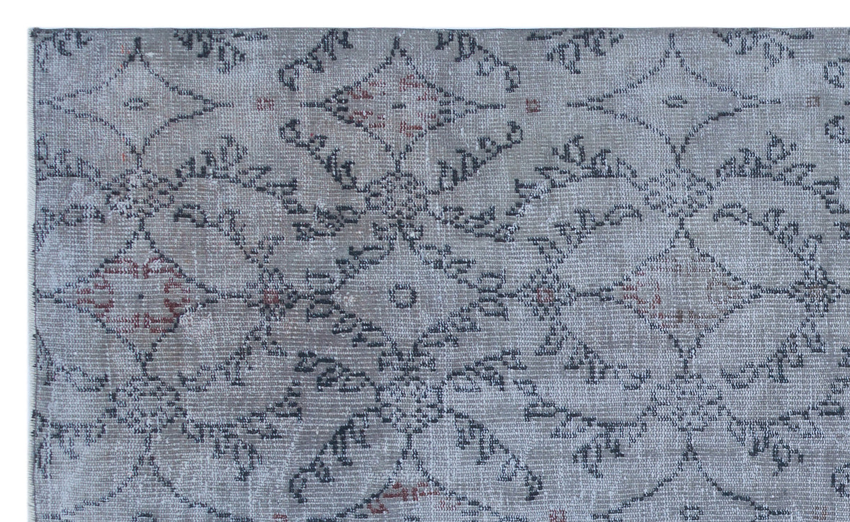 Grey and charcoal distressed rug with a repeating geometric medallion pattern and subtle red accents.