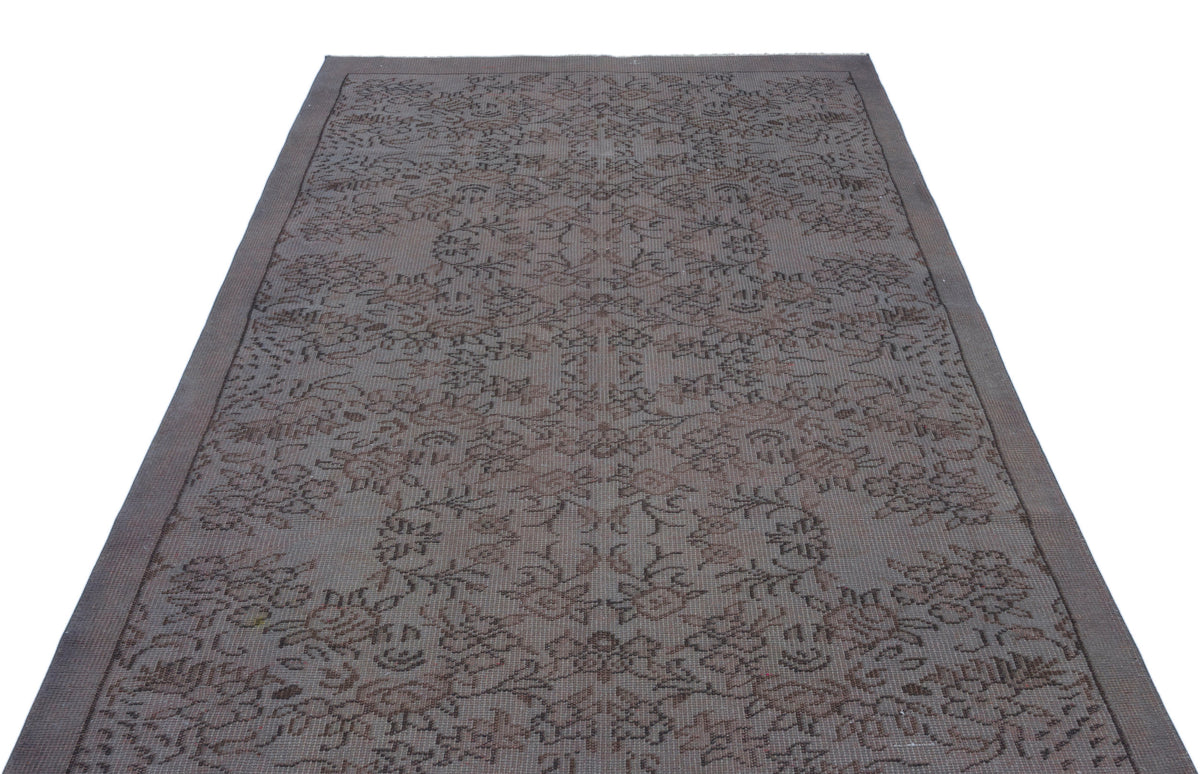 Dark grey and brown rug with a faded, intricate floral medallion pattern on a white background.