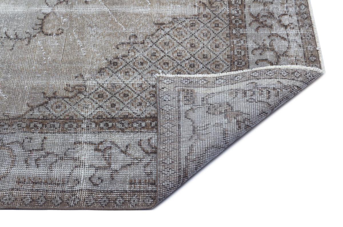 Distressed taupe and grey rug with a geometric diamond and floral border pattern, shown with a folded corner.