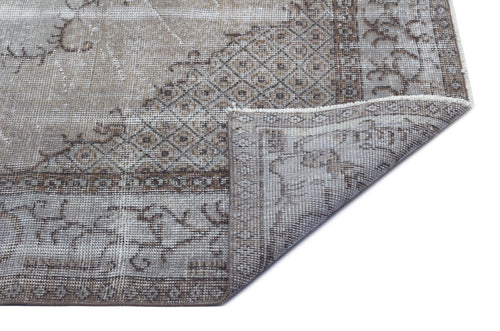 Load image 1 in gallery view. Distressed taupe and grey rug with a geometric diamond and floral border pattern, shown with a folded corner.