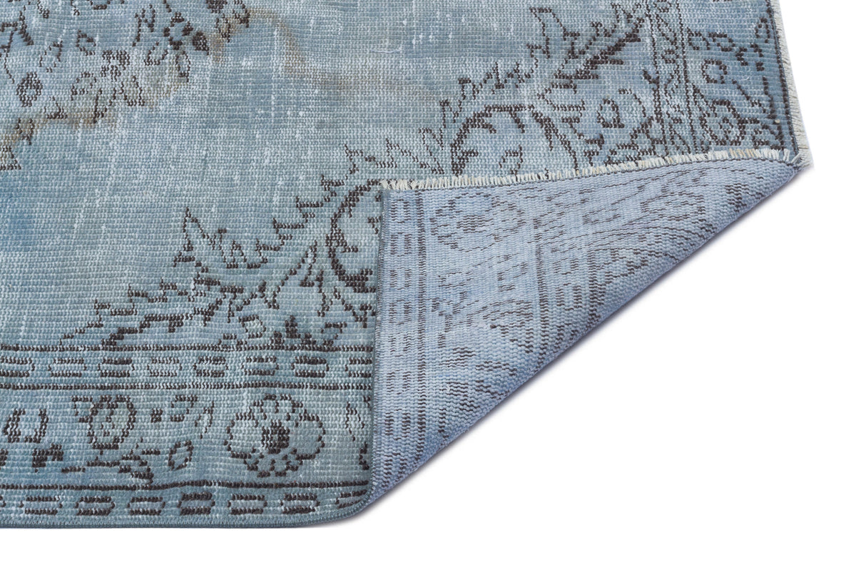 Light blue distressed rug with a dark grey floral medallion pattern, shown with a corner folded over.