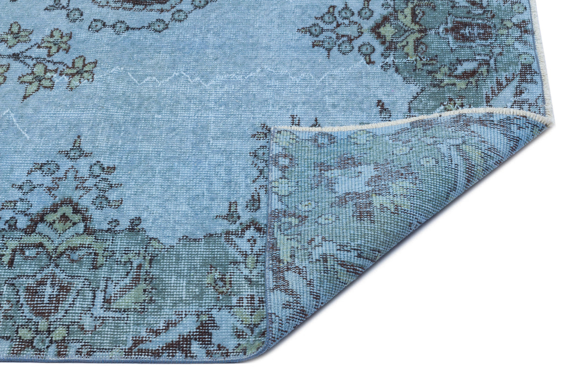Light blue distressed rug with dark brown and sage green floral medallion patterns, shown with a folded corner.