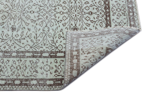 Load image 1 in gallery view. Light green and brown traditional rug with a floral medallion pattern, shown with a corner folded over on white.