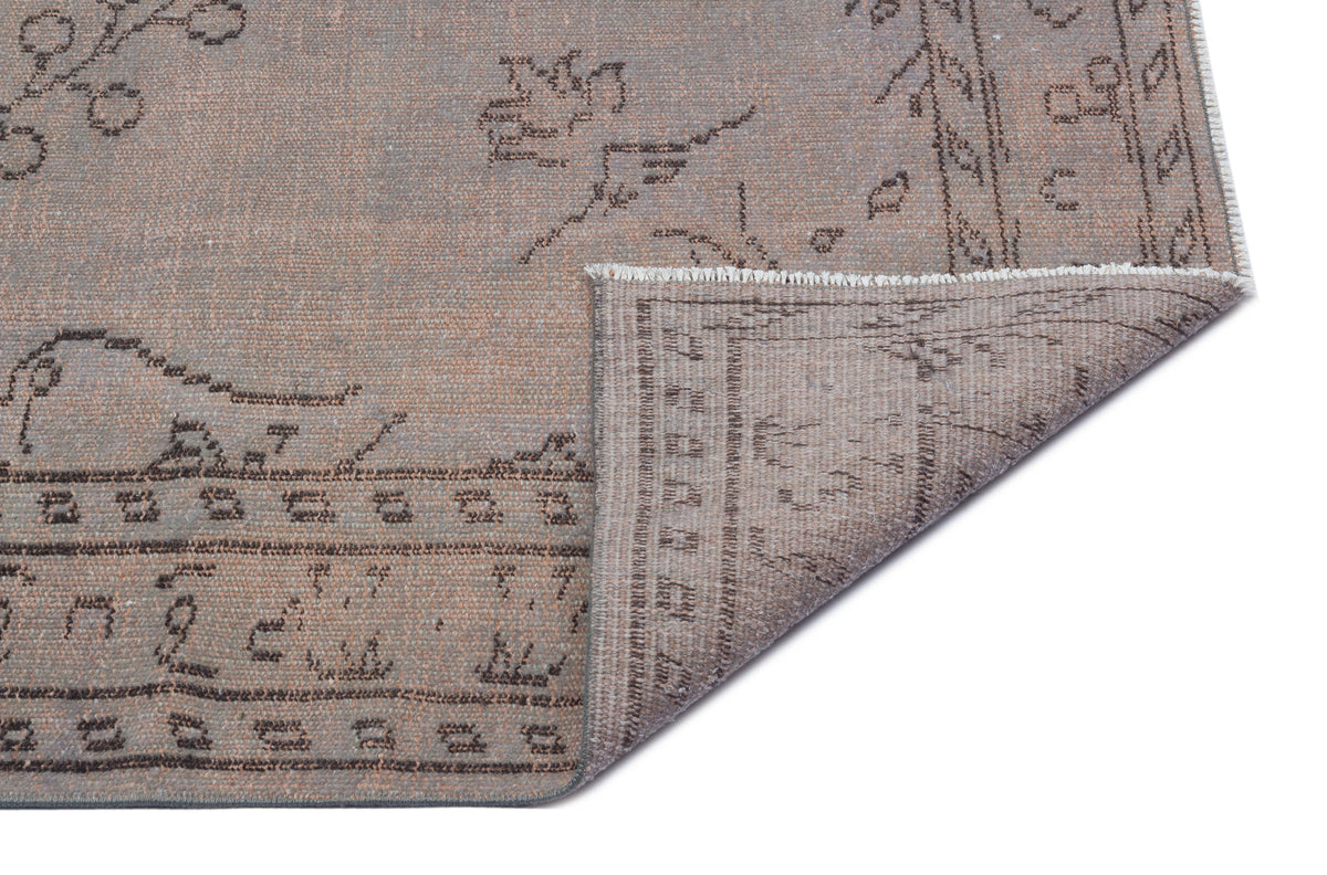 Taupe and grey distressed area rug with a faded traditional border and floral motif, shown with a corner folded over.