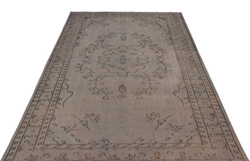 Load image 1 in gallery view. Muted brown vintage-style rug with a central floral medallion and a geometric border pattern on a white background.