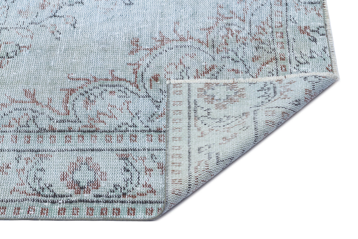 Light blue distressed rug with a faded floral medallion pattern and a folded corner showing the woven backing.