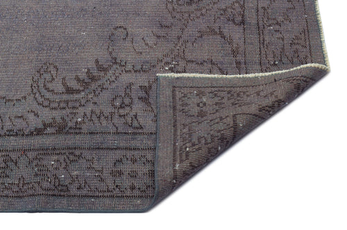 Load image 1 in gallery view. Charcoal grey rug with a faded traditional floral pattern and a folded corner revealing the woven backing.