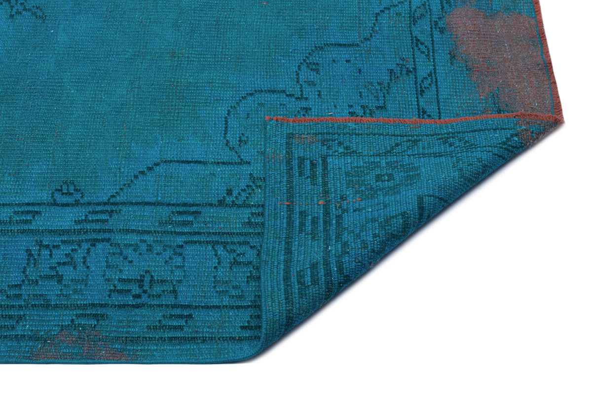 Teal distressed rug with a dark blue linear pattern and a folded corner revealing a rust-colored underside.
