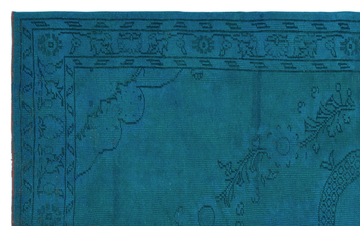 Teal rug with a dark blue linear border and subtle floral corner motifs.