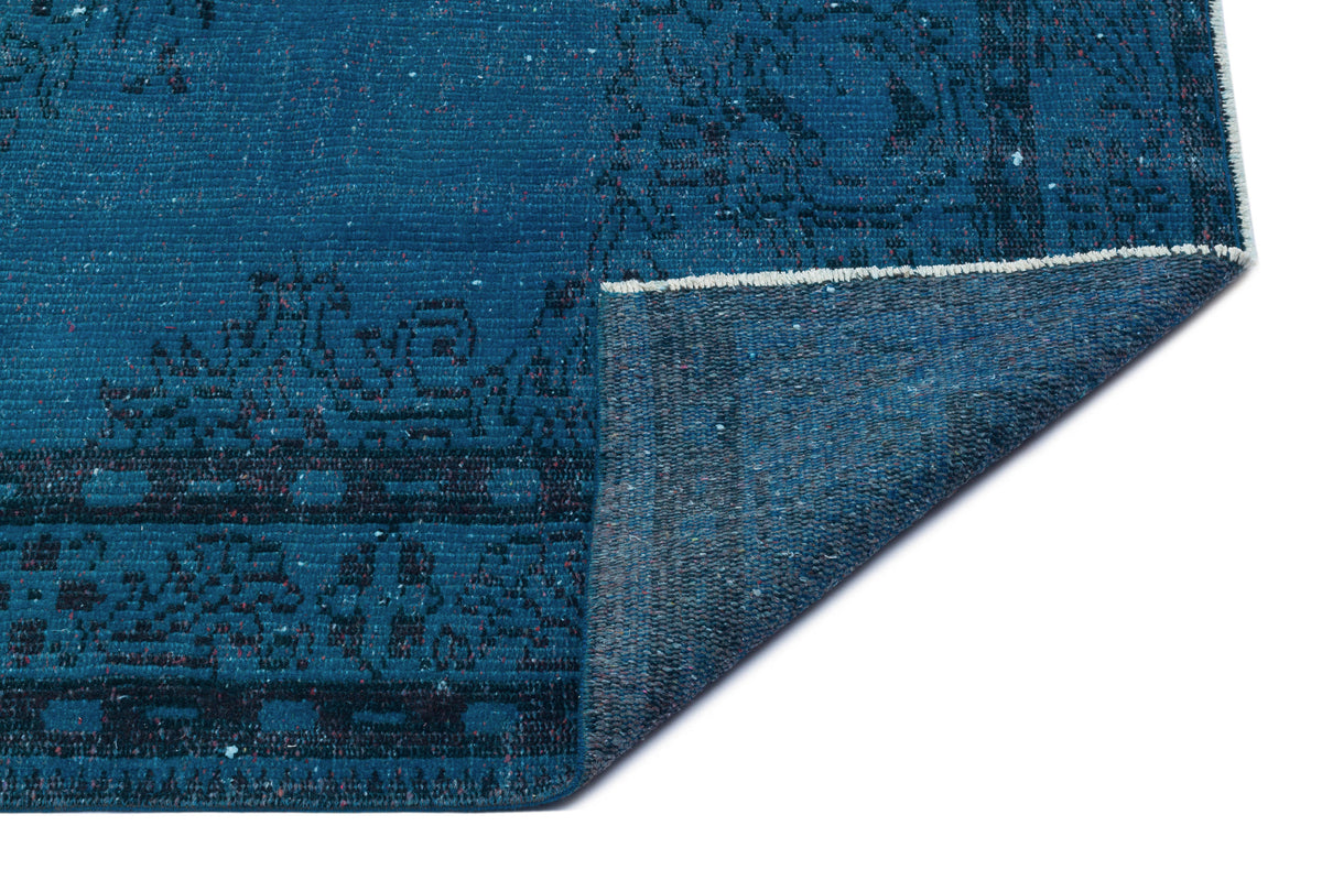 Deep blue distressed rug with a dark geometric border pattern, shown with a folded corner on a white background.