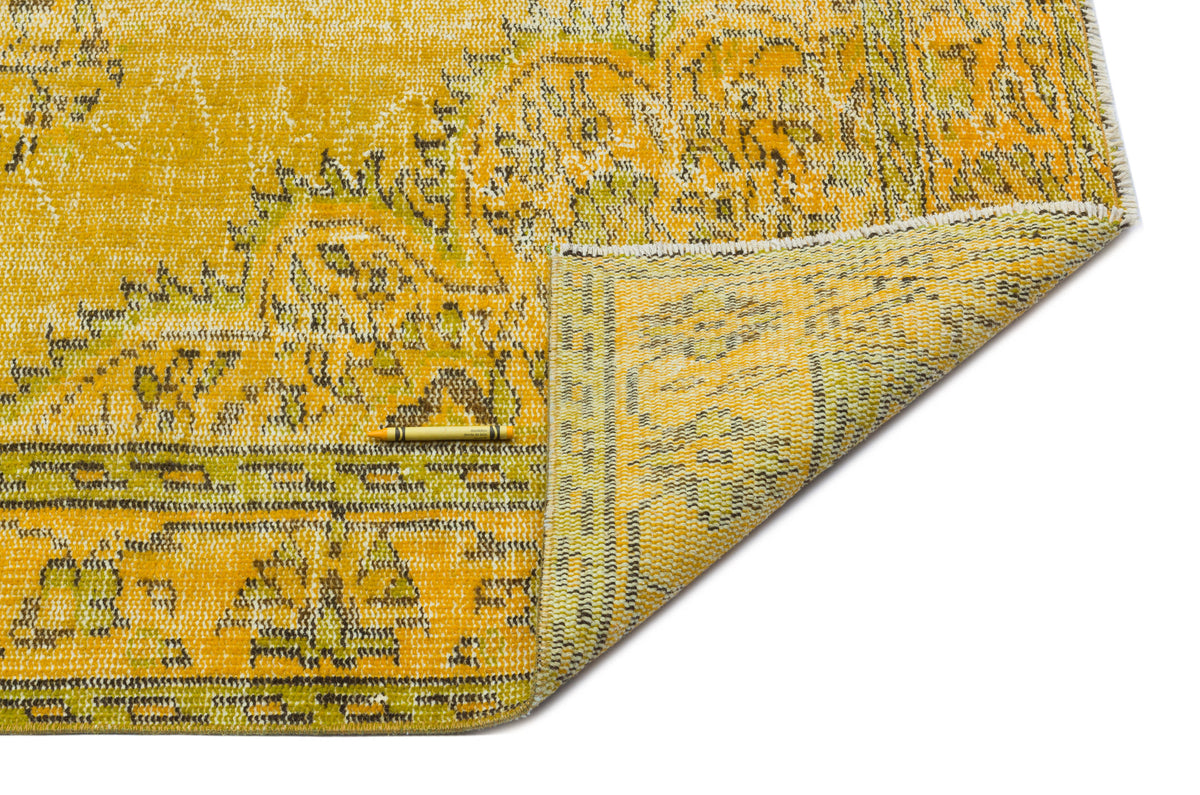 Yellow and green distressed medallion rug with a folded corner, isolated on a white background.