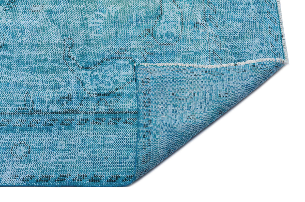 Distressed turquoise and blue rug with a faded traditional pattern, shown with a corner folded over on a white background.