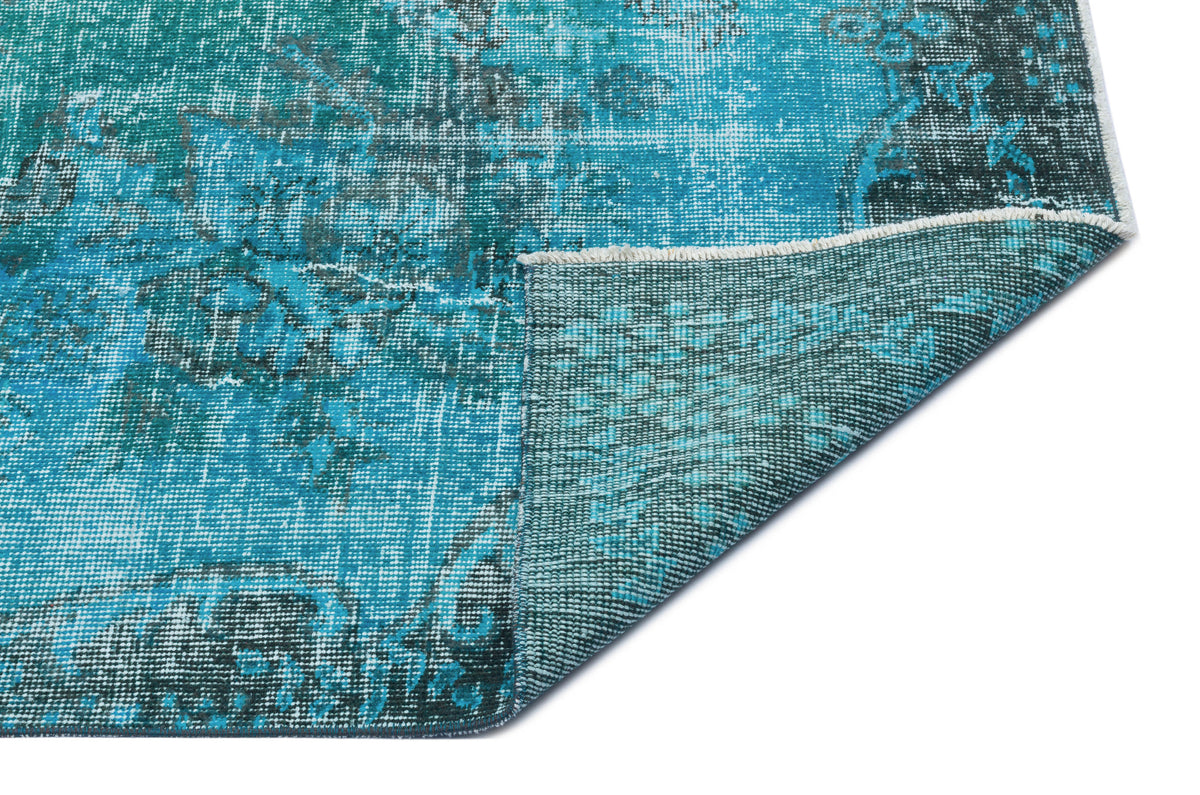 Teal and dark grey distressed rug with a faded traditional pattern, shown with a corner folded over on a white background.